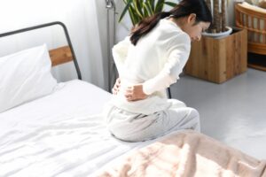 朝ベッドの上で腰を押さえる女性|産後の腰の重だるさ